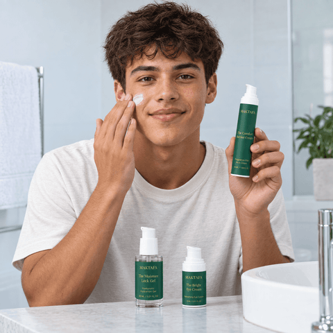 Person applying cream to a cheek while holding a Maktafa bottle at the bathroom basin.