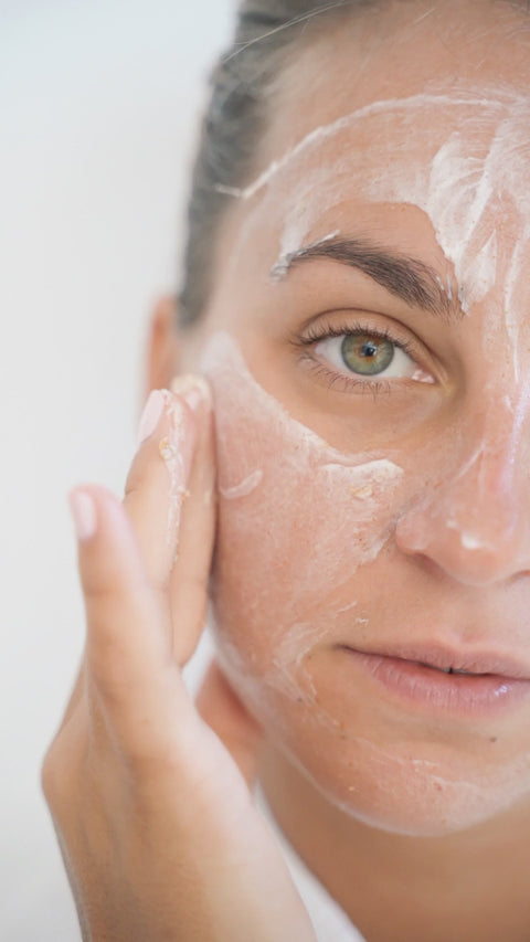 Illustrative close-up video of a person spreading cream over a cheek and forehead.