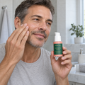 Person applying skincare to a cheek while holding a Maktafa serum bottle.