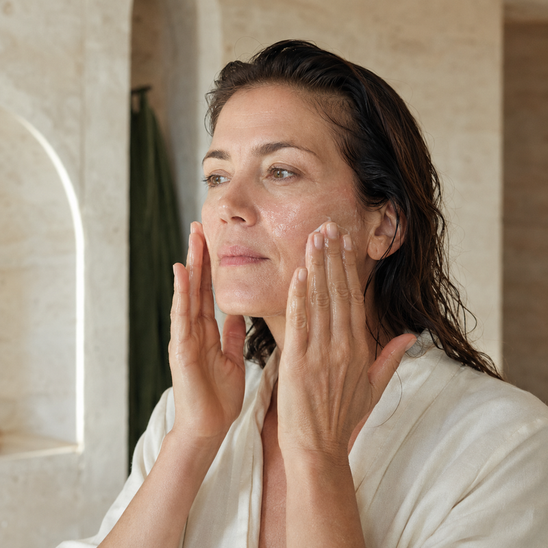 Woman pressing skincare into both cheeks with her fingertips.