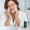 Person massaging cleansing foam over the cheeks, with a Maktafa cleanser beside the basin.
