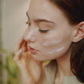 Illustrative video of a person smoothing cream over a cheek with fingertips.